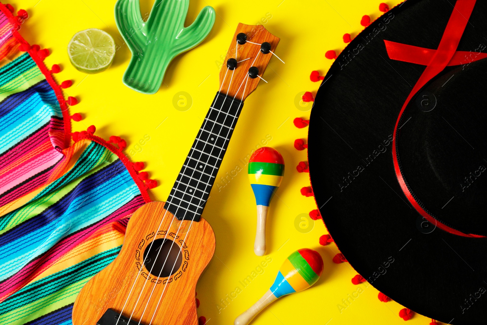 Photo of Flat lay composition with black Flamenco hat, poncho, ukulele and maracas on yellow table