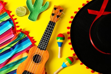 Flat lay composition with black Flamenco hat, poncho, ukulele and maracas on yellow table