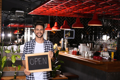 Photo of Young business owner holding sign OPEN in his cafe. Space for text