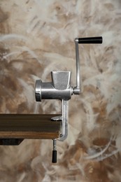 Metal manual meat grinder on wooden table against color background