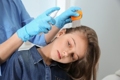 Photo of Doctor using nit comb and spray on girl's hair indoors. Anti lice treatment