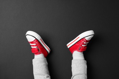Photo of Little child in stylish red gumshoes on black background, top view