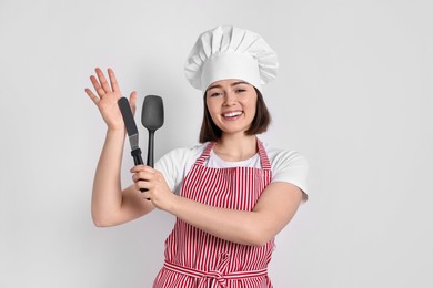 Photo of Happy confectioner holding spatulas on light grey background