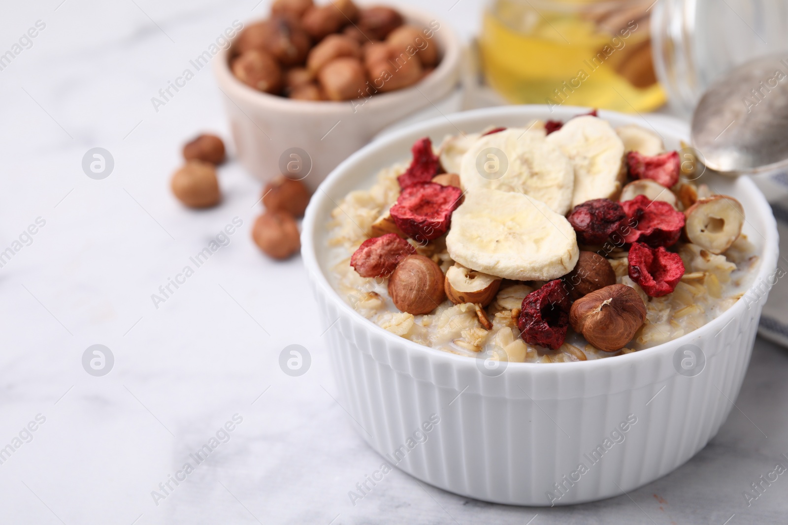 Photo of Delicious oatmeal with freeze dried berries, banana and hazelnuts on white marble table, closeup. Space for text