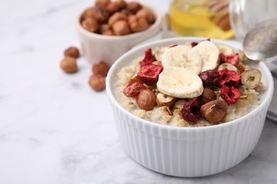 Delicious oatmeal with freeze dried berries, banana and hazelnuts on white marble table, closeup. Space for text