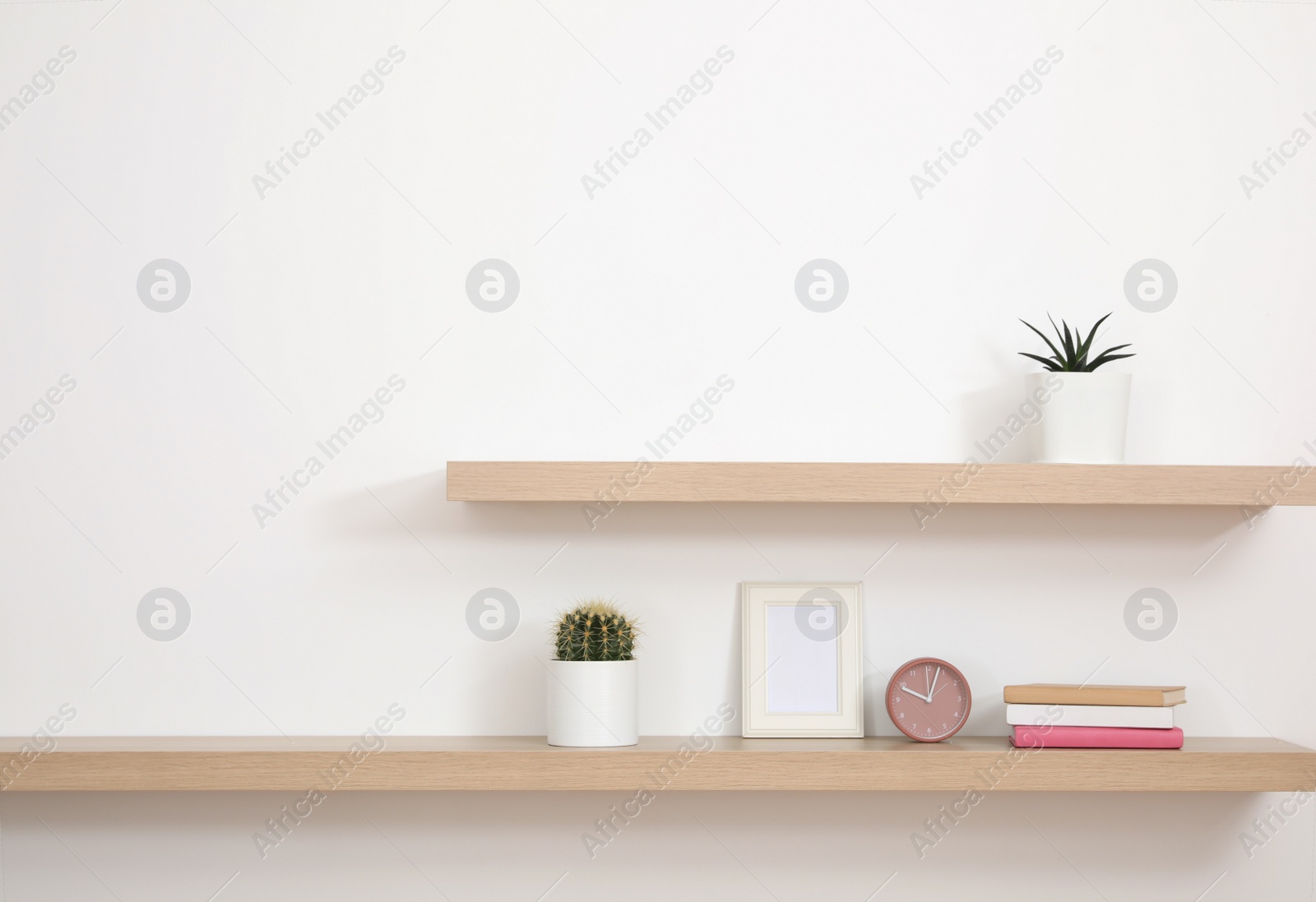 Photo of Wooden shelves with books and decorative elements on light wall