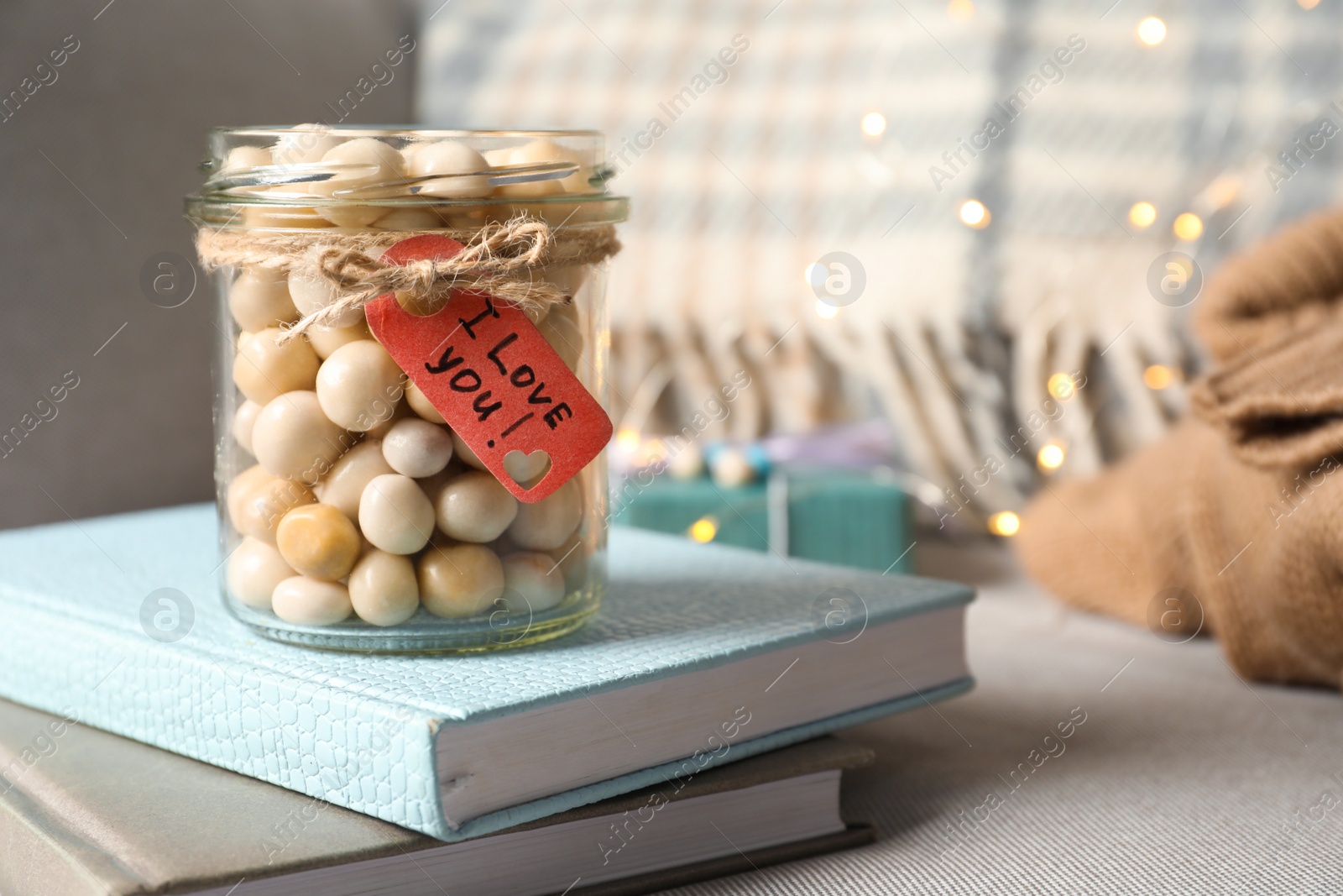 Photo of Greeting card with phrase I Love You tied to jar full of candies on table