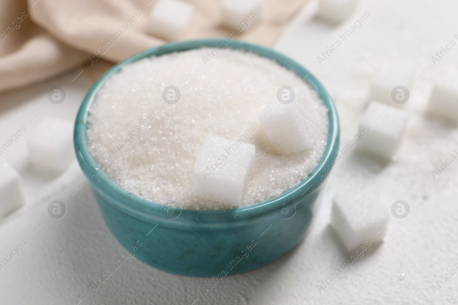 Photo of Different types of sugar in bowl on white table, closeup