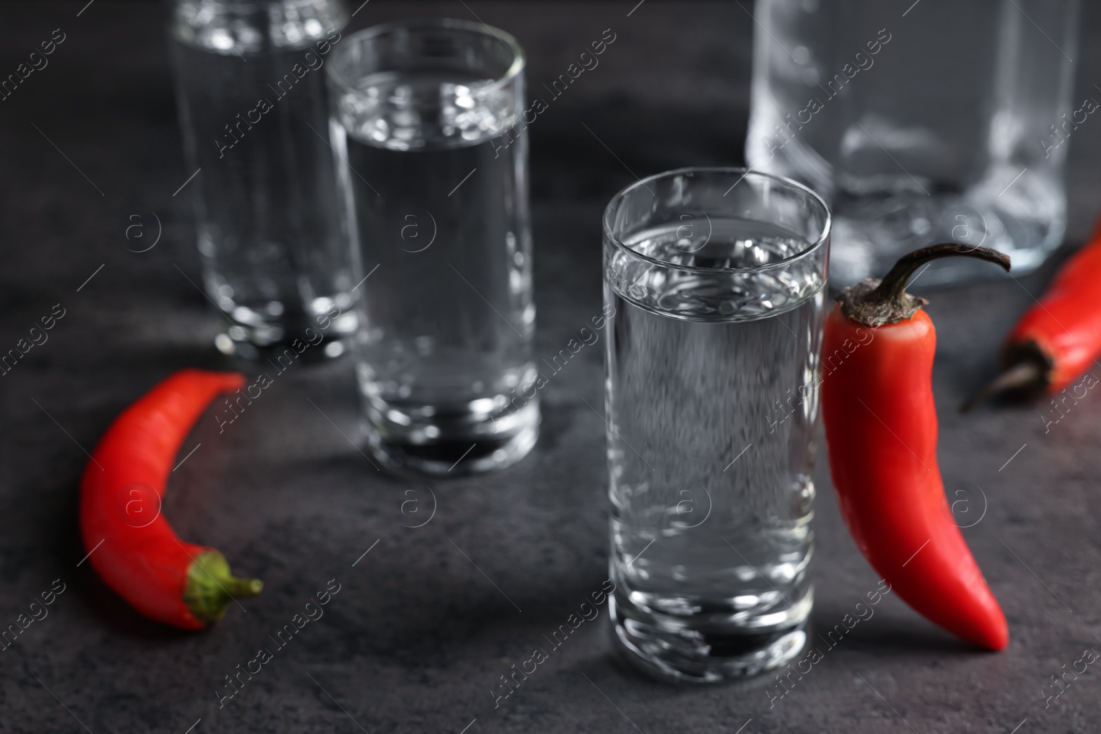 Photo of Red hot chili peppers and vodka on grey table