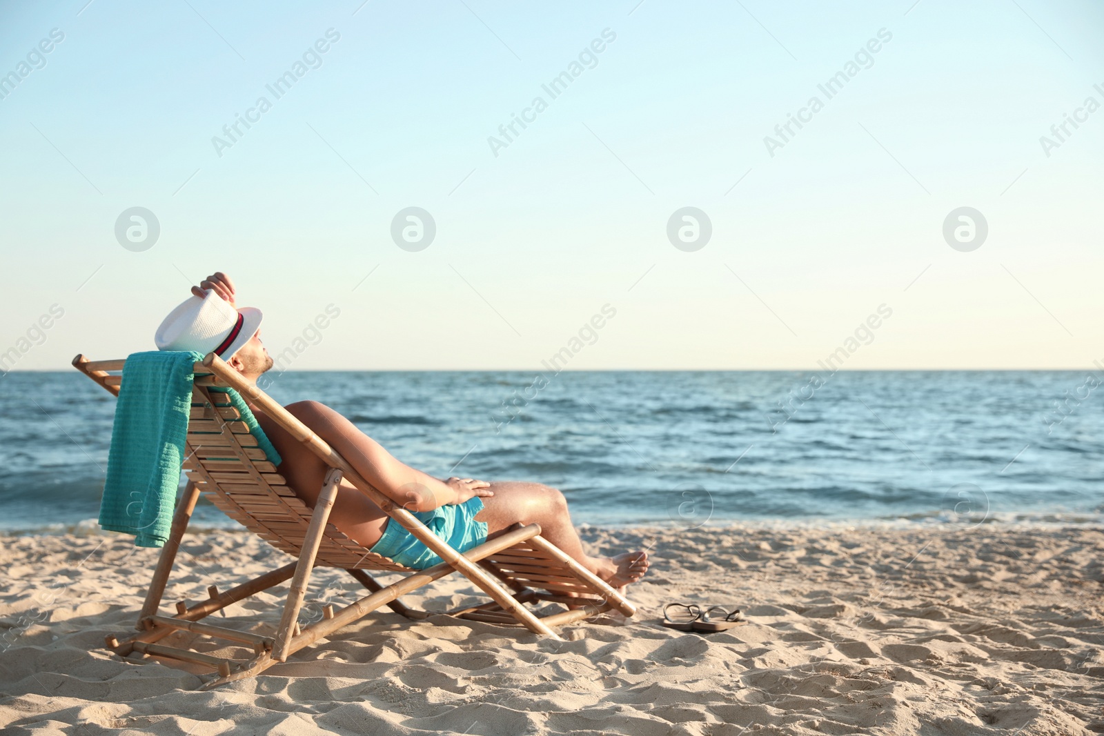 Photo of Young man relaxing in deck chair on beach near sea