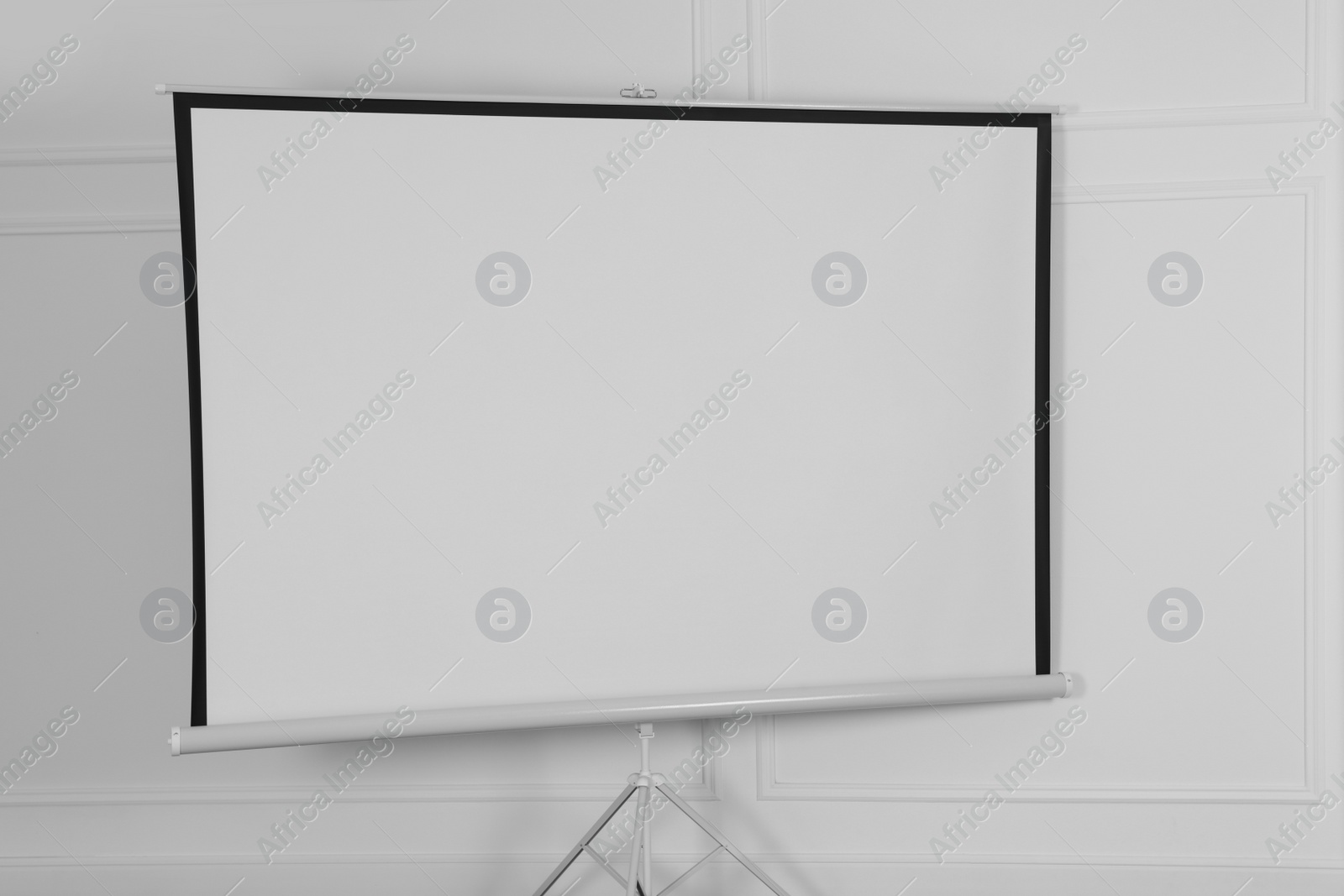 Photo of Blank projection screen near white wall indoors. Space for design