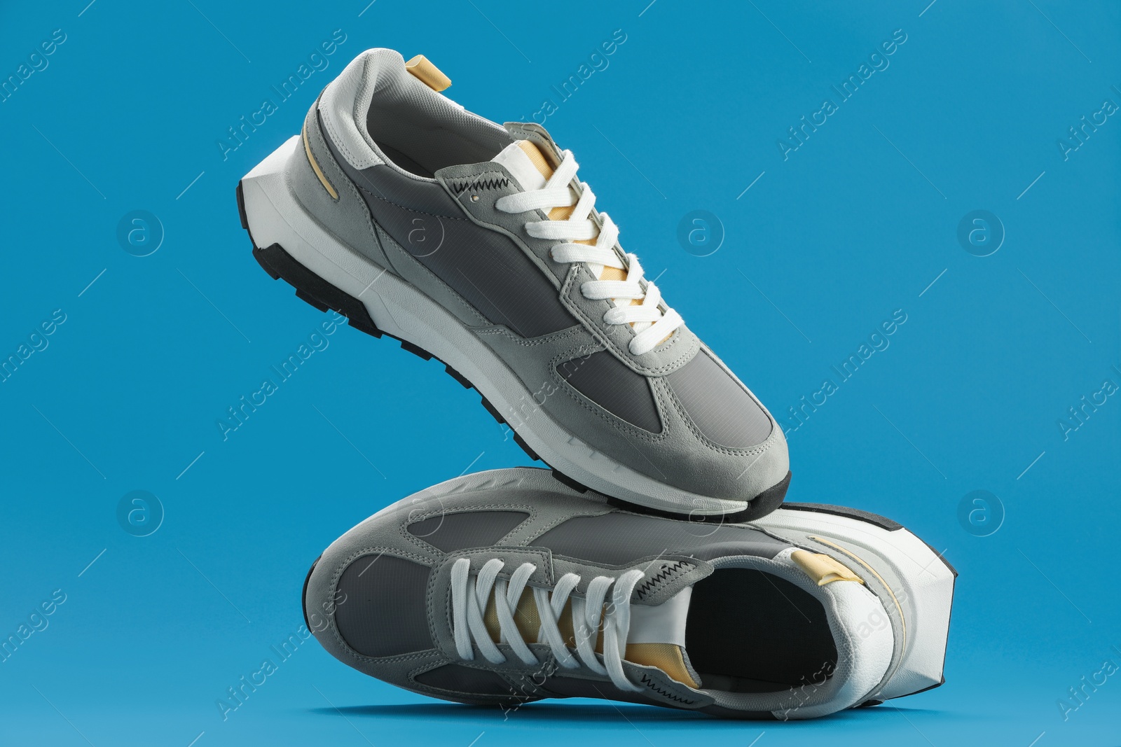 Photo of Pair of stylish grey sneakers falling on blue background