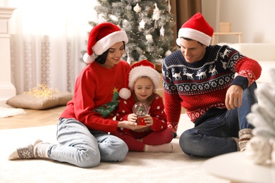 Photo of Family in Santa hats playing with snow globe at home