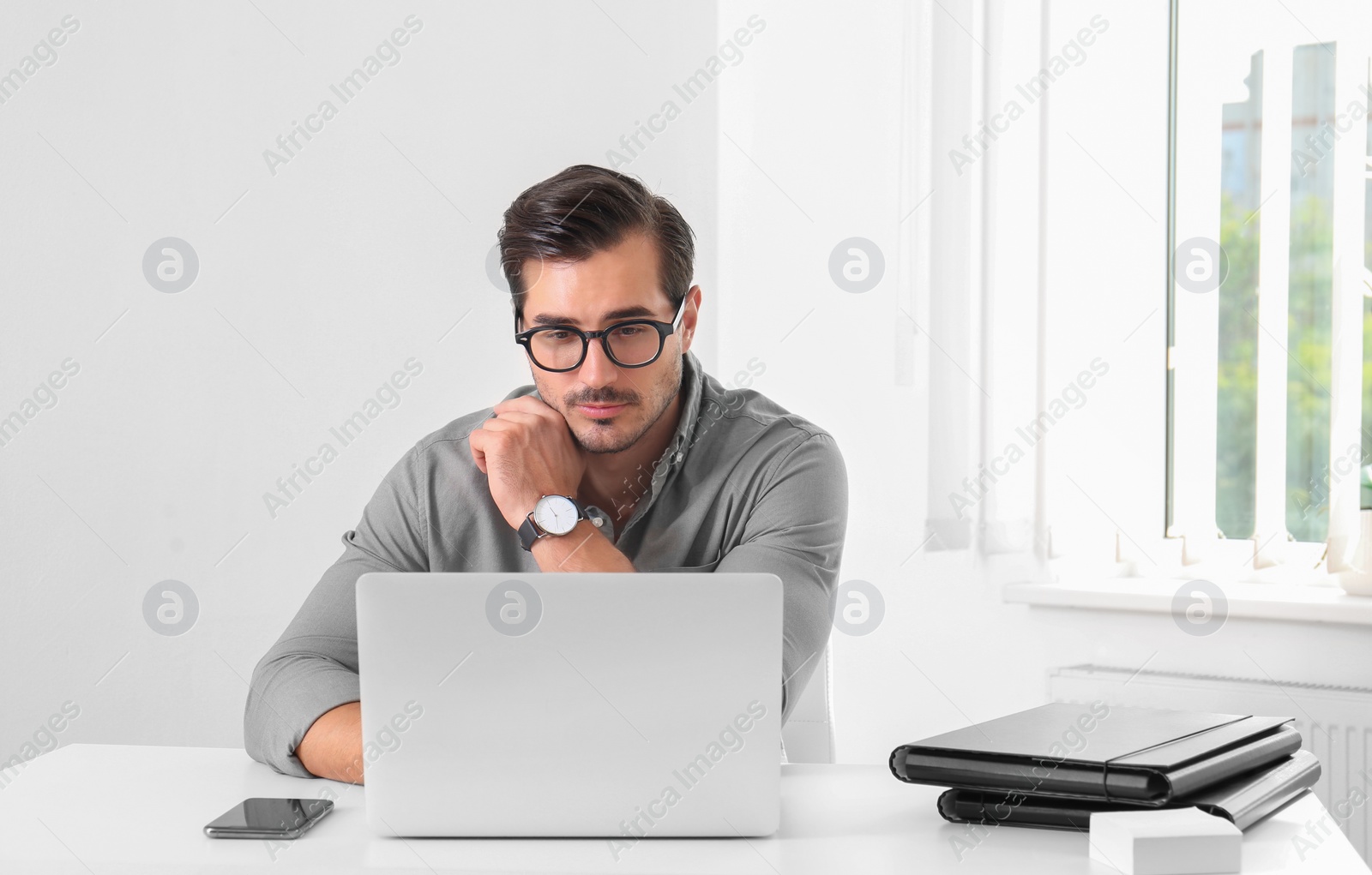 Photo of Handsome young man working with laptop at table in office