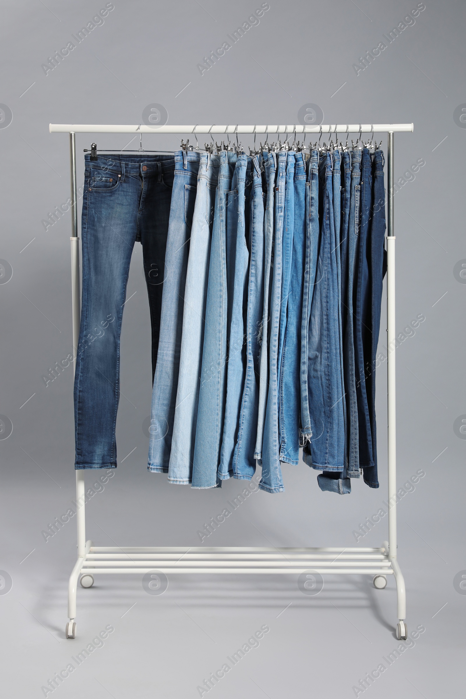 Photo of Rack with different jeans on grey background