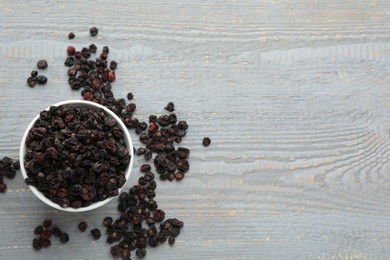 Photo of Dried black currants and bowl on grey wooden table, flat lay. Space for text