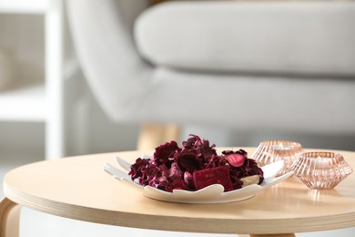 Photo of Aromatic potpourri of dried flowers and candles on coffee table indoors