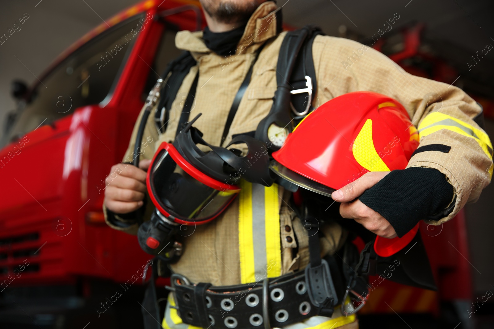 Photo of Firefighter in uniform with helmet and mask near red fire truck at station, closeup