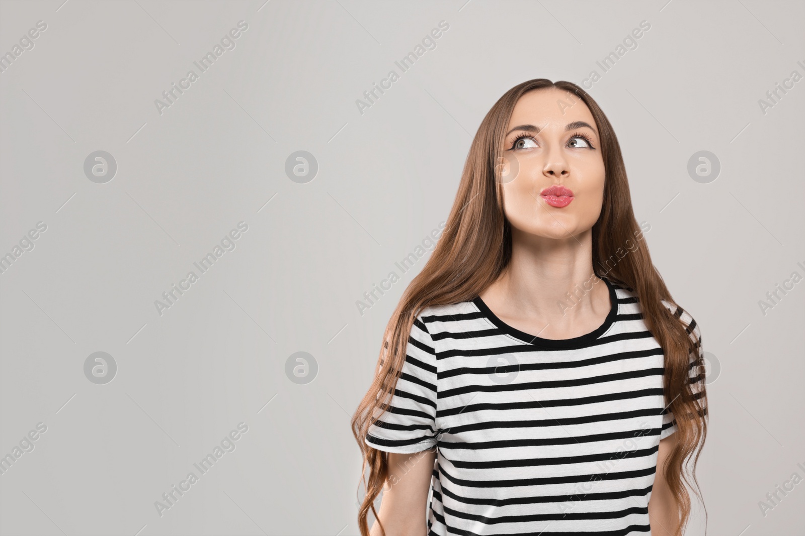 Photo of Beautiful young woman blowing kiss on light grey background, space for text