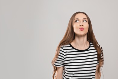 Beautiful young woman blowing kiss on light grey background, space for text