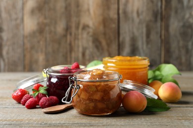 Jars with different jams and fresh fruits on wooden table