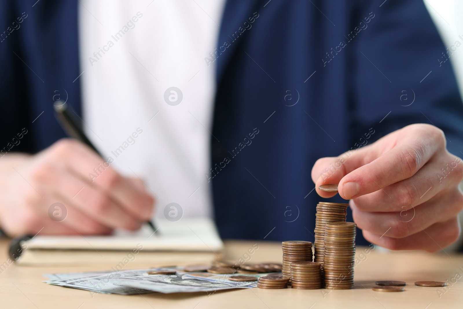 Photo of Financial savings. Man stacking coins while writing down notes at table, closeup