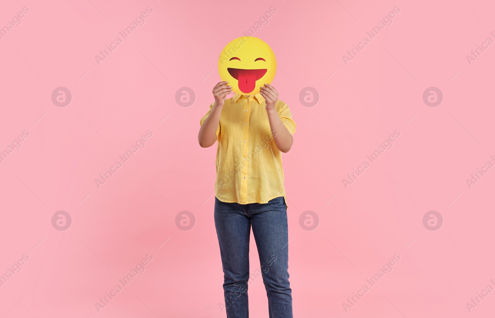 Photo of Woman covering face with emoticon sticking out tongue on pink background