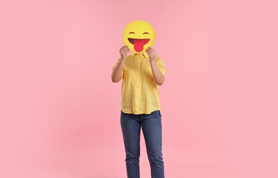 Photo of Woman covering face with emoticon sticking out tongue on pink background