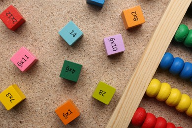 Wooden cubes with numbers and multiplications near abacus on fiberboard, flat lay