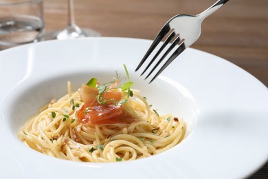 Photo of Eating tasty spaghetti with prosciutto and microgreens at table, closeup. Exquisite presentation of pasta dish