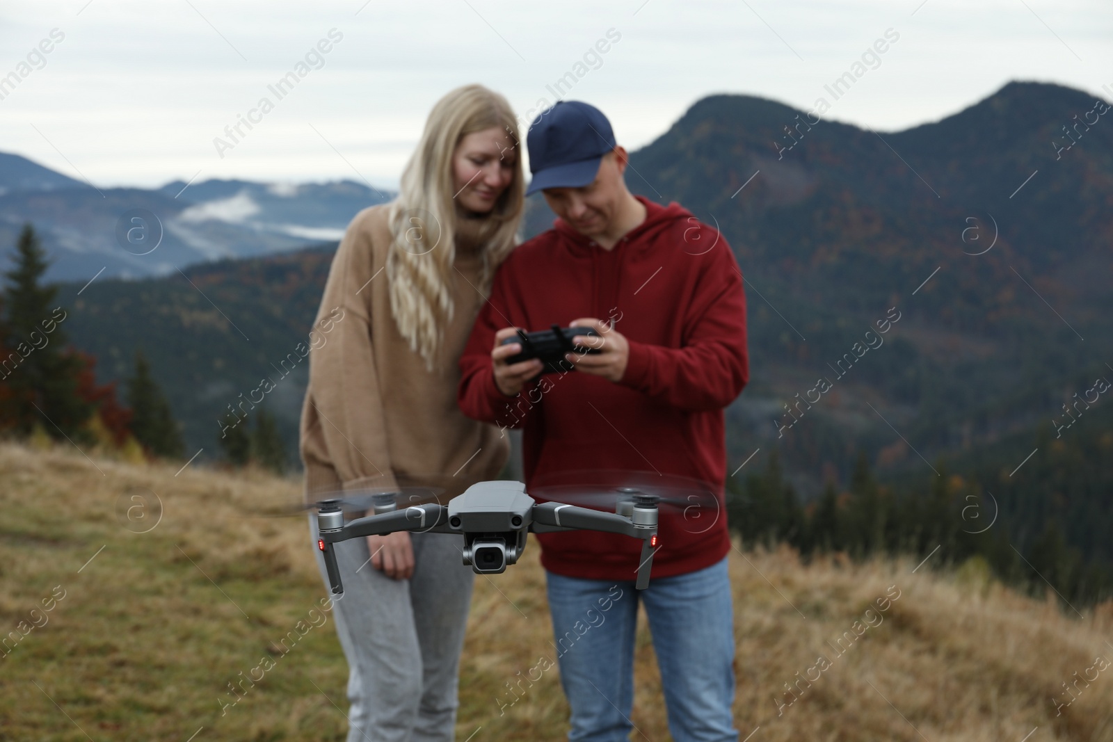 Photo of Young couple operating modern drone with remote control in mountains