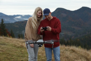 Young couple operating modern drone with remote control in mountains