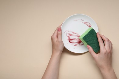 Woman washing dirty plate with sponge on beige background, top view. Space for text