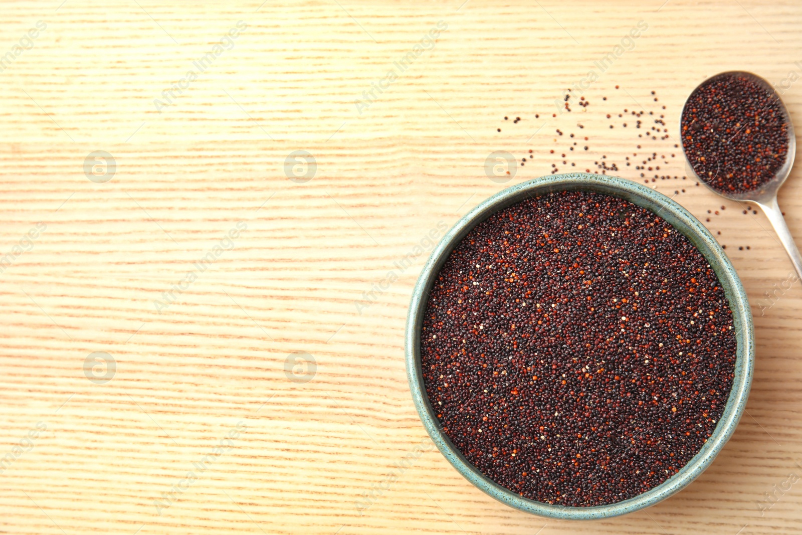 Photo of Spoon and bowl with black quinoa on wooden background, top view. Space for text