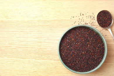 Spoon and bowl with black quinoa on wooden background, top view. Space for text