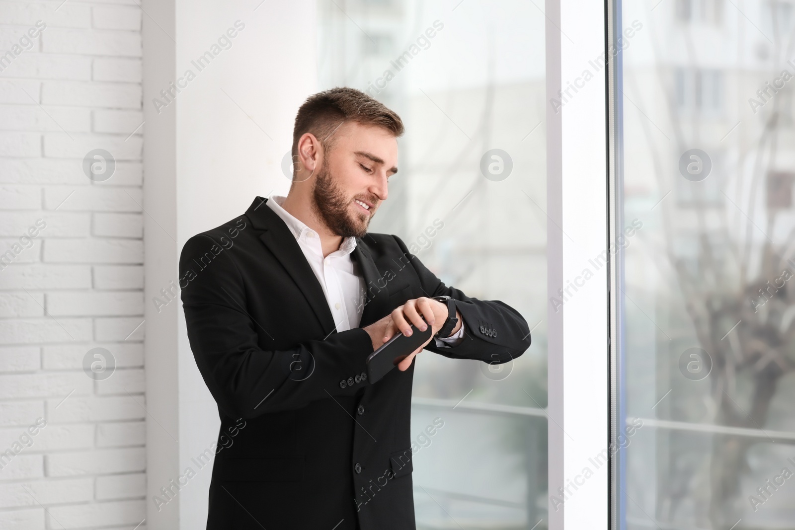 Photo of Young businessman checking time near window at home
