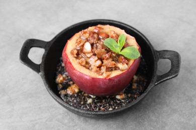 Photo of Tasty baked apple with nuts, honey and mint in baking dish on gray table, closeup