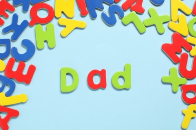 Word Dad made of magnetic letters on light blue background, flat lay. Learning alphabet