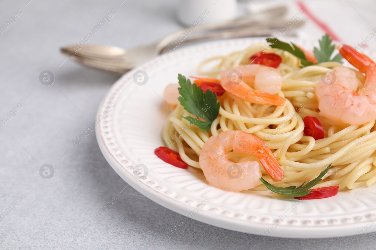 Photo of Tasty spaghetti with shrimps, chili pepper and parsley on grey table, closeup. Space for text