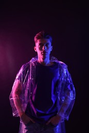 Photo of Young man wearing clear coat on dark background in neon lights