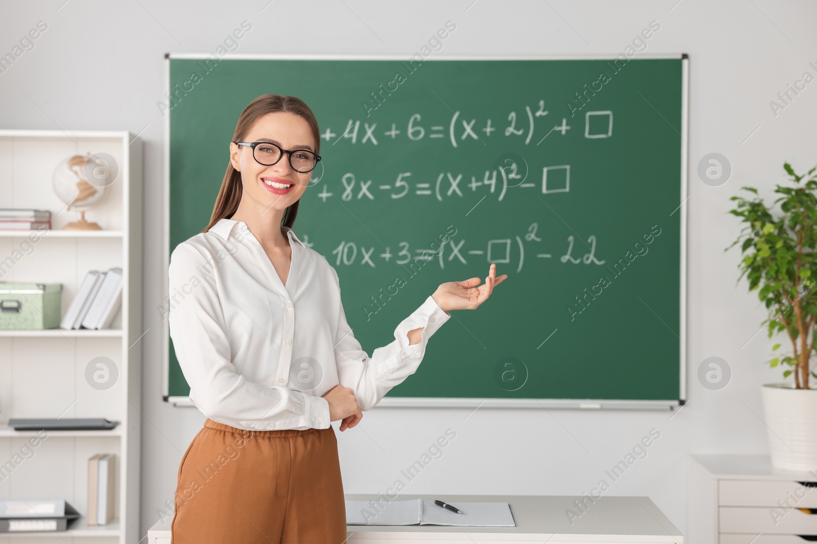 Photo of Young math’s teacher explaining mathematical equations near chalkboard in classroom