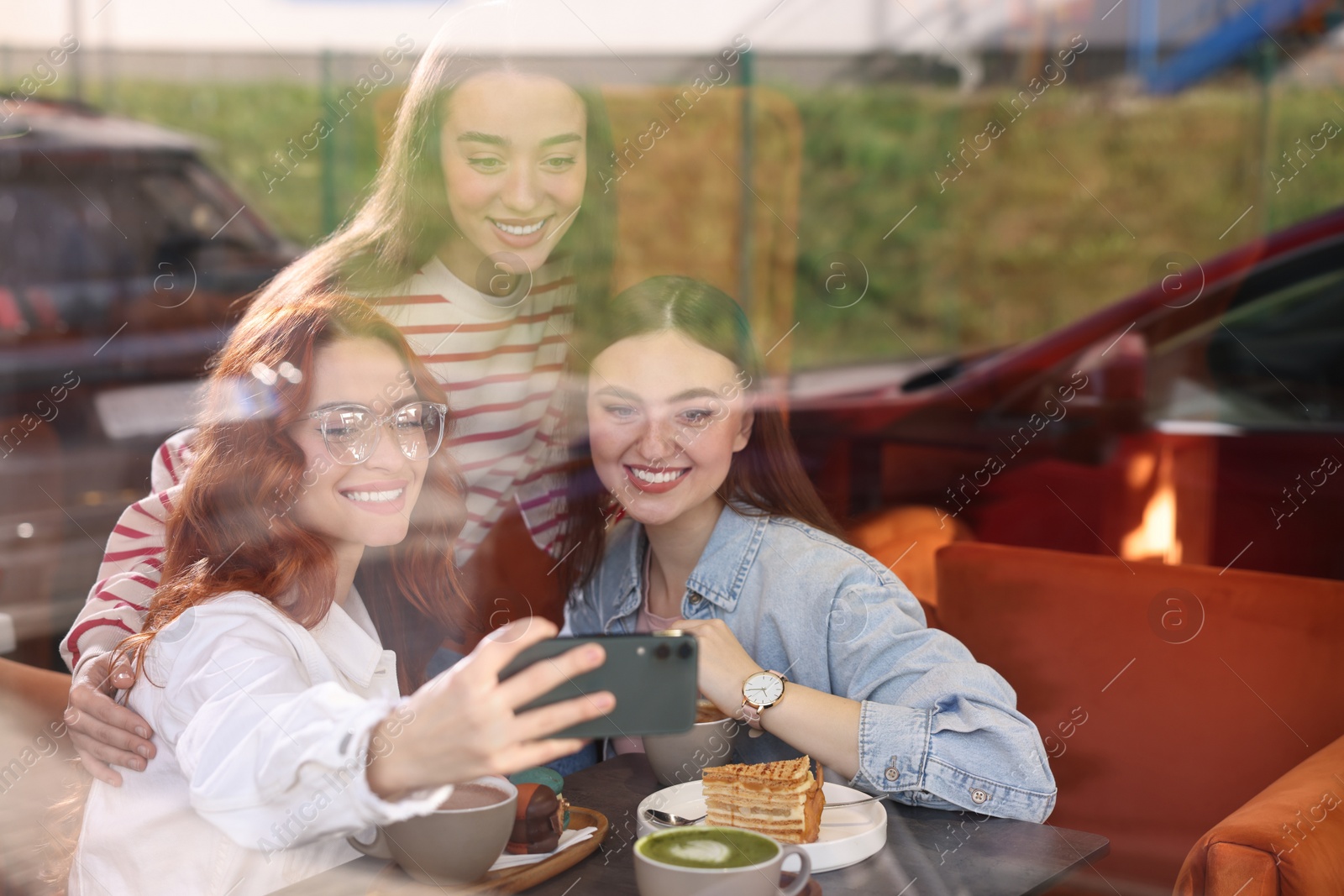 Photo of Happy friends taking selfie in cafe, view through window