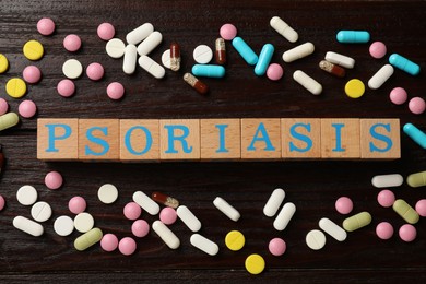 Photo of Word Psoriasis made of cubes with letters and pills on wooden table, flat lay