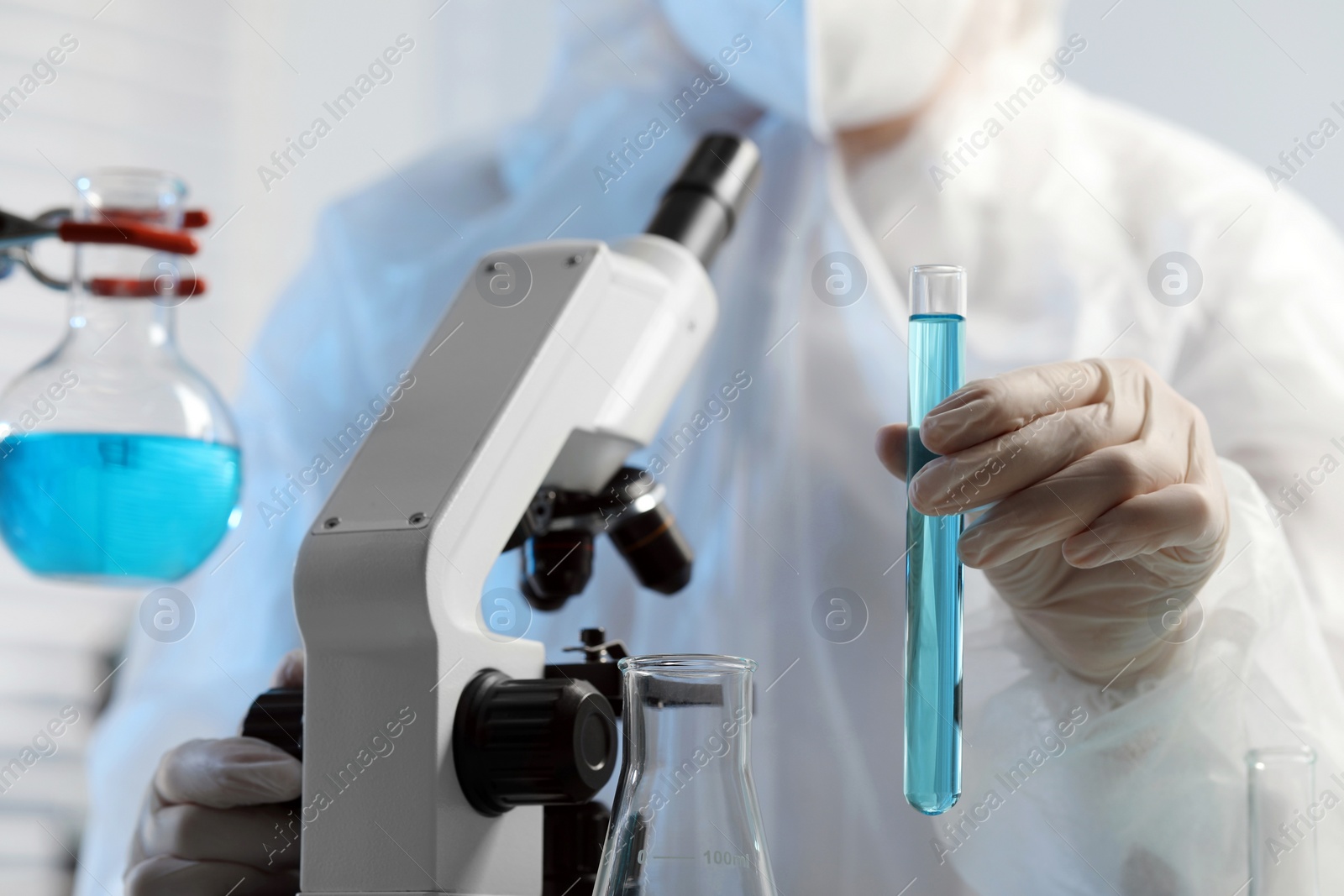 Photo of Scientist with test tube of light blue liquid and microscope in laboratory, closeup