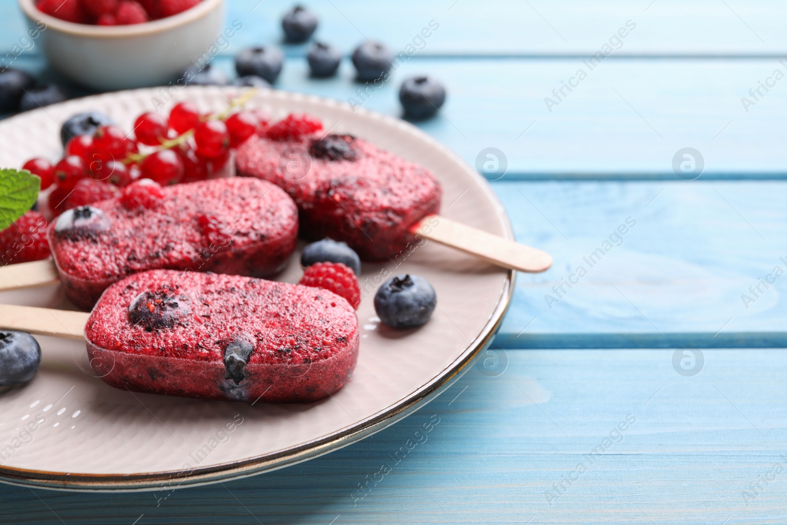 Photo of Plate of tasty berry ice pops on light blue wooden table, space for text. Fruit popsicle