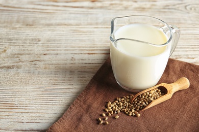 Photo of Scoop with hemp seeds and glass jug of milk on wooden table