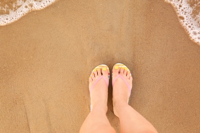 Photo of Top view of woman with stylish flip flops on sand near sea, space for text. Beach accessories