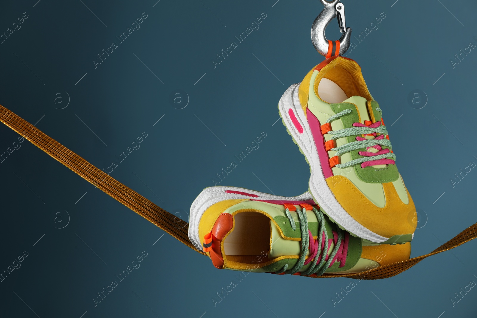 Photo of Pair of stylish colorful sneakers on rope against blue background