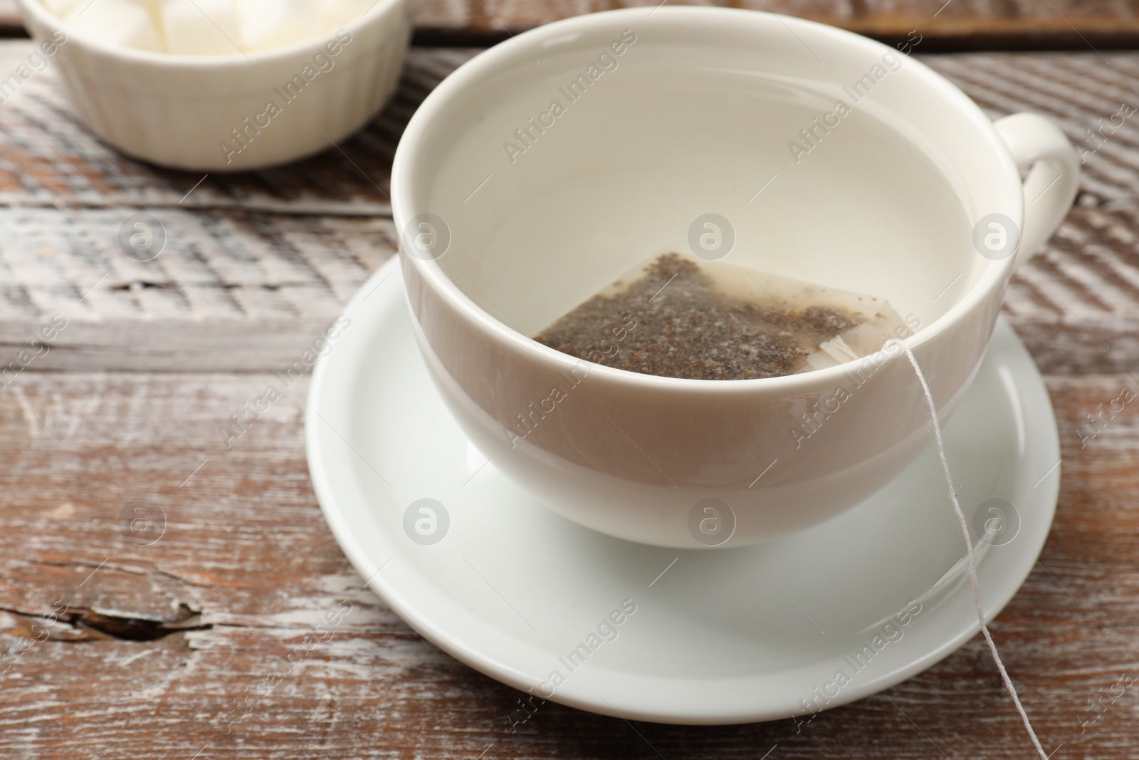 Photo of Tea bag in cup with hot water on wooden rustic table, closeup