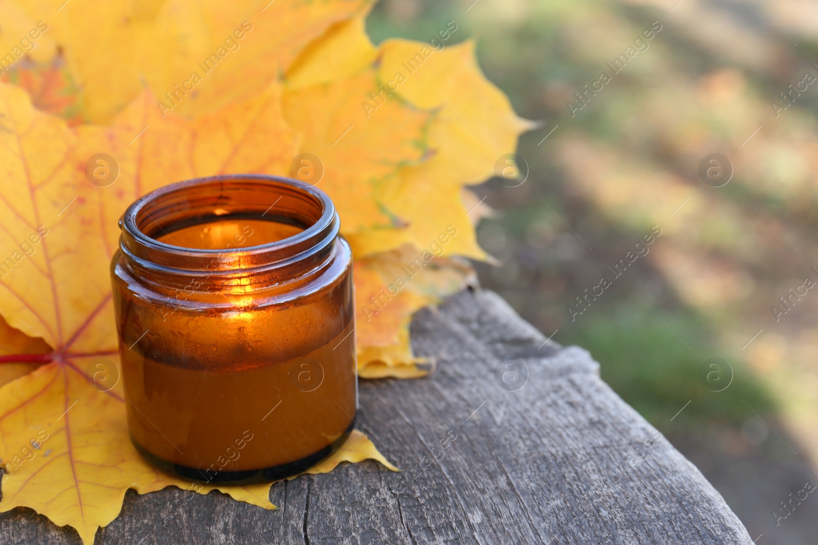 Photo of Burning candle and beautiful dry leaves on wooden surface outdoors, closeup with space for text. Autumn atmosphere